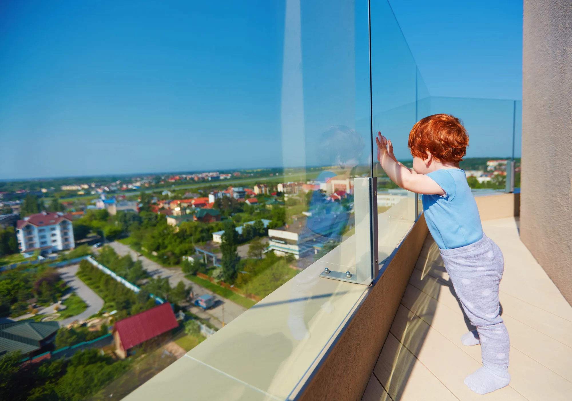 Child safely standing behind a glass balcony balustrade